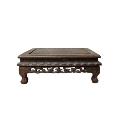 A traditional display stand, carved from dense, dark wood. It features a flat, smooth top surface, surrounded by a moulded frame. The lower section is characterised by its richly carved skirt featuring ornamental motifs, openwork and volutes, resting on four sturdy, curved cabriole-style legs. Available for hire for events, advertising, films and TV series.