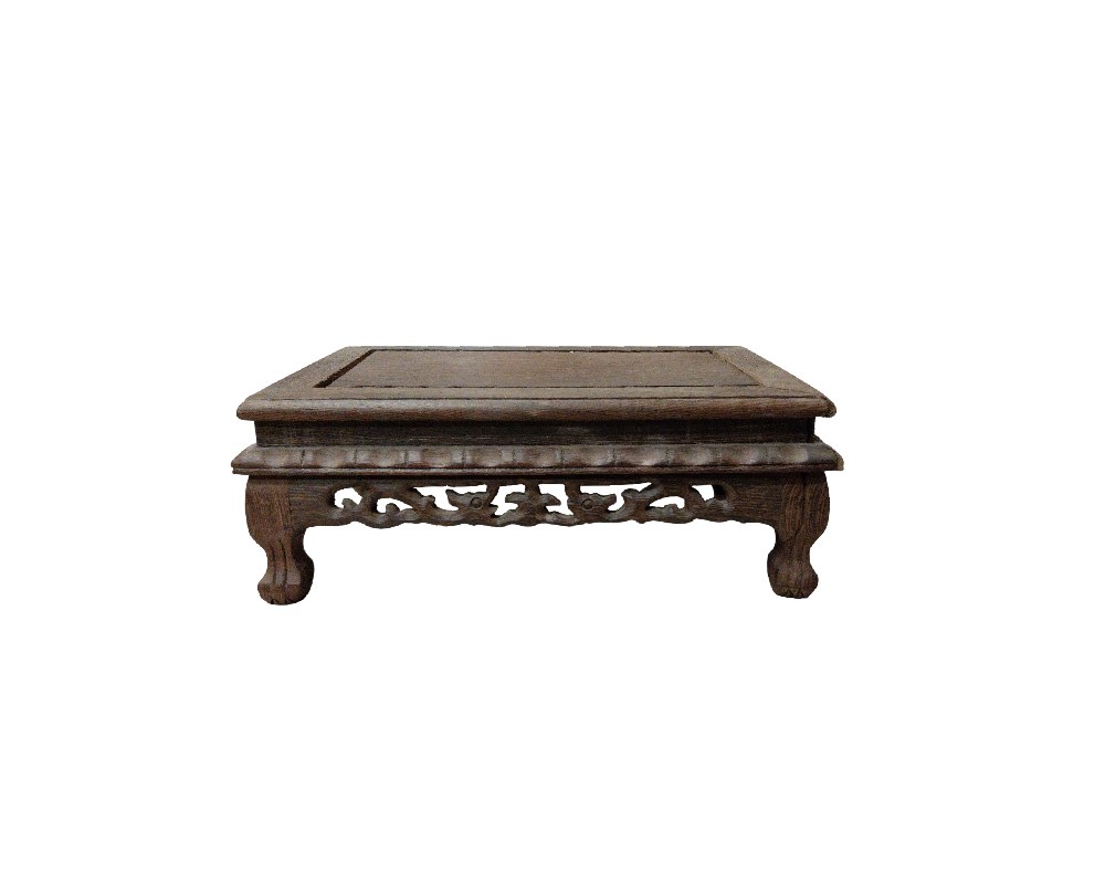 A traditional display stand, carved from dense, dark wood. It features a flat, smooth top surface, surrounded by a moulded frame. The lower section is characterised by its richly carved skirt featuring ornamental motifs, openwork and volutes, resting on four sturdy, curved cabriole-style legs. Available for hire for events, advertising, films and TV series.