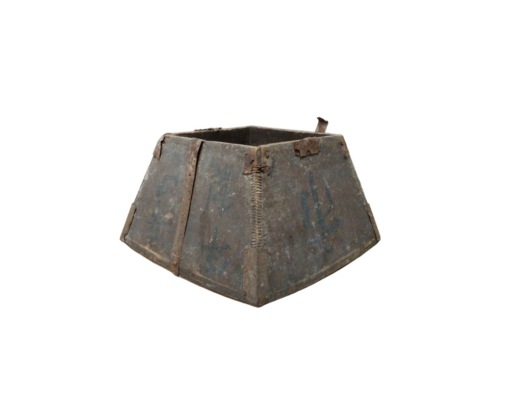 caja de madera de forma troncopiramidal, caracterizada por una estructura ensanchada en la base, refuerzos de metal oxidado en las esquinas y juntas, y caracteres tradicionales impresos en sus caras laterales alquiler para eventos, publicidad, peliculas y series