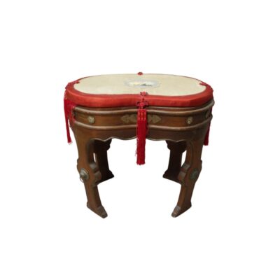 A low wooden stool with a traditional design, featuring ornate curved legs with metal fittings, a padded seat in light and red tones, and hanging cord and red fringe details. Available for hire for events, advertising, films and TV series.