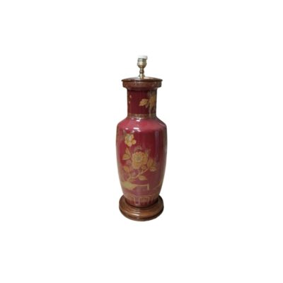 lámpara de mesa con base de cerámica de color rojo burdeos, caracterizada por un cuerpo alargado de estilo oriental, elegantes decoraciones florales pintadas en tonos dorados y ocres, un casquillo superior y una sólida base de madera alquiler para eventos, publicidad, peliculas y series