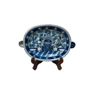 Oval porcelain tray decorated using the traditional blue-on-white technique, featuring a detailed central motif of landscapes, ceremonial vessels and floral elements; available for hire for events, advertising, films and TV series