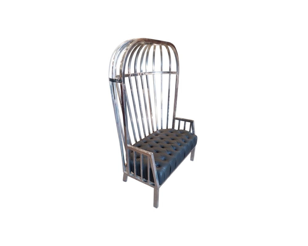 Se distingue por una estructura metálica alta que simula los barrotes de una jaula y un asiento tapizado en color oscuro con técnica de capitoné, combinando un estilo industrial con elegancia decorativa alquiler para eventos, publicidad, peliculas y series