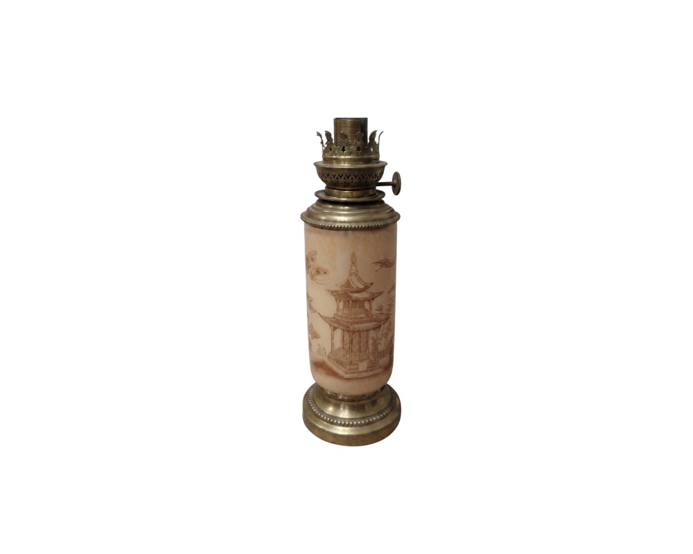 A table lamp with a cylindrical body in light colours, featuring delicate engravings or illustrations in a traditional Oriental style depicting pagodas and elements of nature, framed by a base and an upper burner mechanism; available for hire for events, advertising, films and TV series