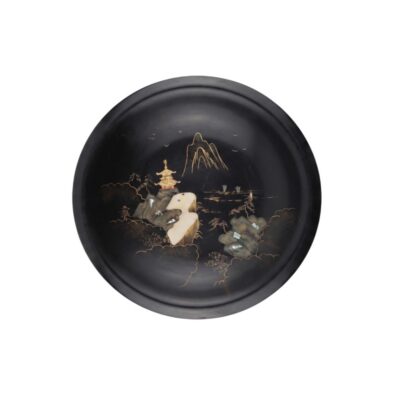A round, deep plate with a dark surface and a smooth finish, characterised by intricate decoration on the base depicting a traditional landscape featuring mountains, a pagoda and natural elements, highlighted in golden tones and inlays; available for hire for events, advertising, films and TV series