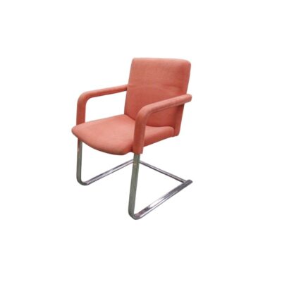 An elegant period chair with a modern design, characterised by a continuous cantilevered tubular metal frame with a chrome finish; the seat, backrest and armrests are upholstered in salmon-orange fabric. Available for hire for events, advertising, films and TV series.
