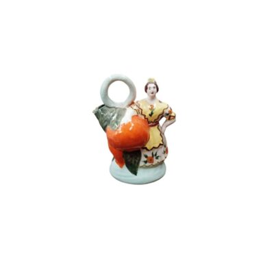 A polychrome ceramic figurine depicting a traditional female figure standing next to a large basket of fruit in shades of orange and green foliage, featuring a circular handle at the top and a pedestal base; available for hire for events, advertising, films and TV series