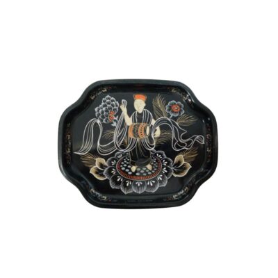 pequeña bandeja de metal con acabado lacado en color negro y bordes de forma lobulada o festonada, caracterizada por una detallada decoración central de inspiración asiática que representa a una figura tradicional con túnica y tambor sobre un soporte floral, rodeada de motivos vegetales y cintas estilizadas en tonos blancos, naranjas y dorados alquiler para eventos, publicidad, peliculas y series