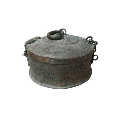 caja de metal de forma circular y aspecto envejecido, caracterizado por una superficie completamente decorada con elaborados grabados y perforaciones de patrones geométricos y florales, una tapa superior con anillas de sujeción y argollas laterales alquiler para eventos, publicidad, peliculas y series