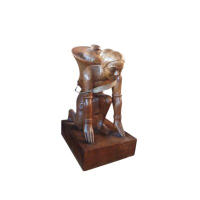 A polished wooden sculpture depicting a human figure in a straining pose, resting on their hands and knees and carrying a container or vessel on their back, secured with a strap; available for hire for events, advertising, films and TV series