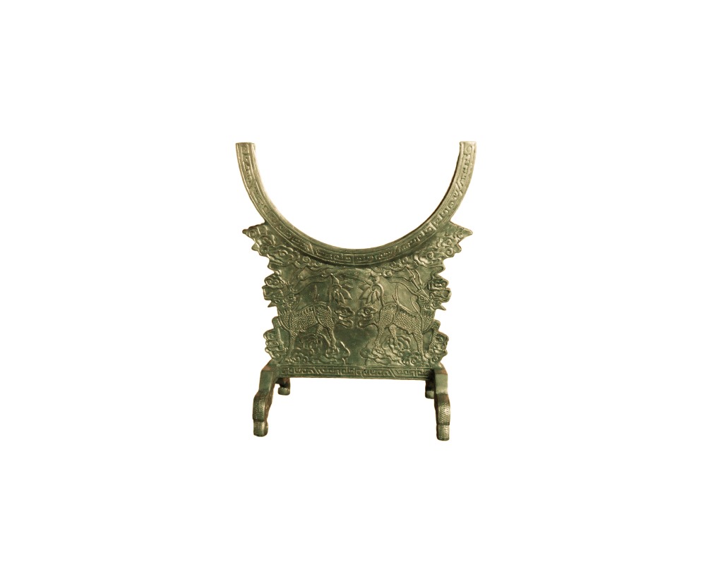 cuna vertical de metal con un acabado envejecido en tonos verdosos, caracterizado por un diseño cóncavo superior y una sección central decorada con relieves detallados que muestran animales o criaturas mitológicas enfrentadas entre motivos de nubes y cenefas tradicionales alquiler para eventos, publicidad, peliculas y series