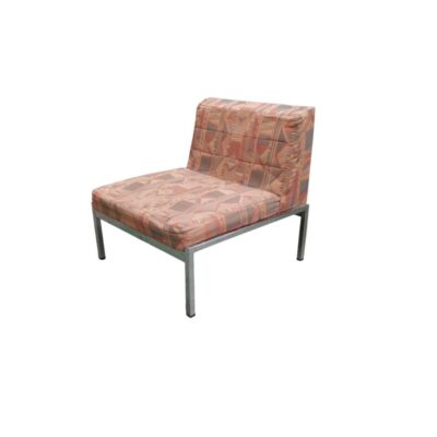 Vintage armless armchair, characterised by a wide, padded seat and backrest upholstered in fabric with a distinctive retro-inspired geometric pattern in shades of pink and earthy tones, supported by a sturdy, straight-lined metal frame. Available for hire for events, advertising, films and TV series