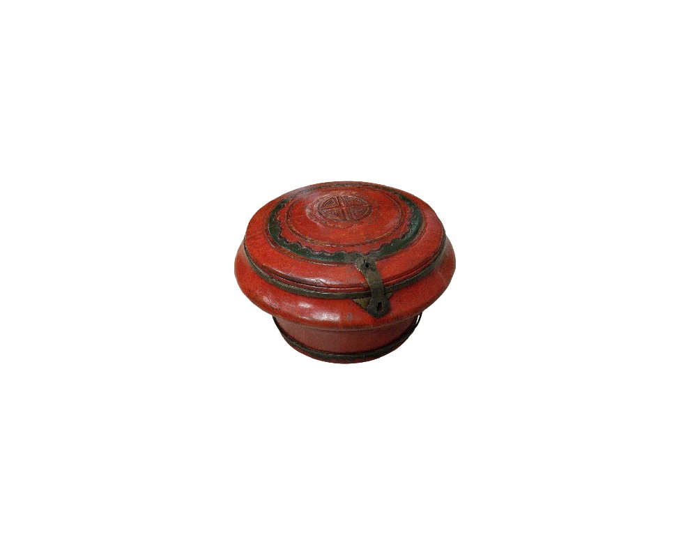 A circular wooden container with a red-toned finish and ornamental details on the lid, characterised by a flared top, engraved geometric motifs and a metal latch on the front; available for hire for events, advertising, films and TV series