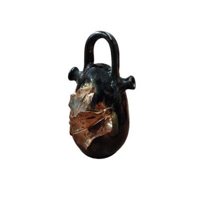 An elongated, ovoid ceramic vessel, featuring a high bridge handle, side spouts and a surface covered in a rich, dark glaze with a glossy finish; available for hire for events, advertising, films and TV series
