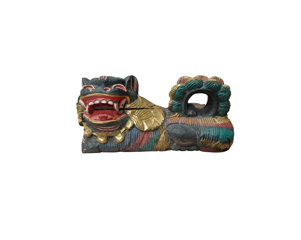 A carved wooden sculpture depicting a traditional mythological creature, a guardian lion or foo dog, characterised by a reclining body in a dynamic pose, polychrome details in dark, red, green and gold tones, and an expressive design; available for hire for events, advertising, films and TV series
