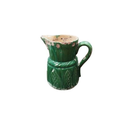 A rustic ceramic milk jug characterised by a cylindrical body decorated with raised motifs on its lower section, a side handle and a pronounced spout; available for hire for events, advertising, films and TV series