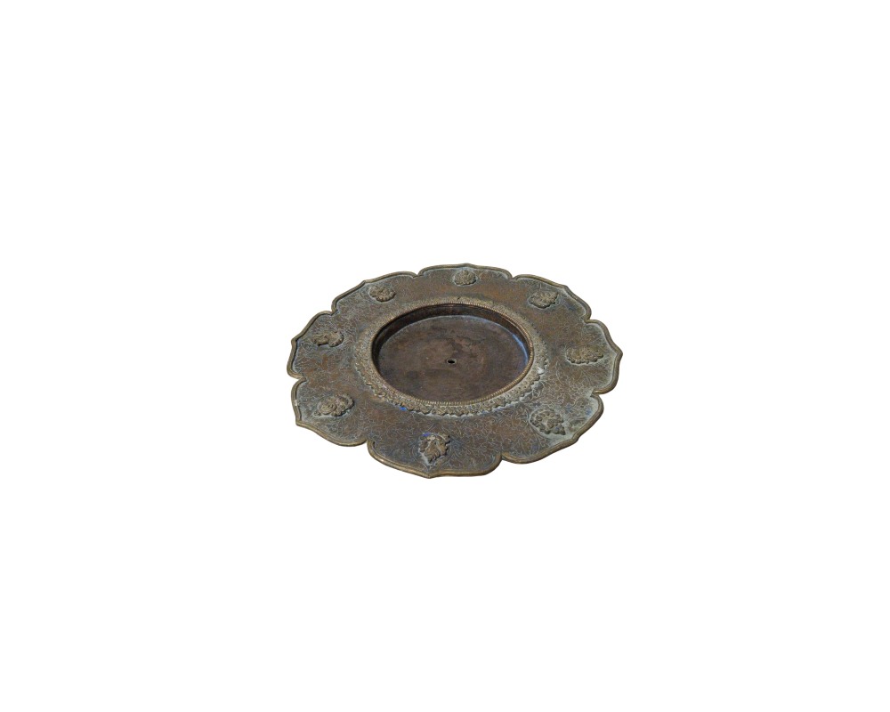 A metal plate with an antique appearance and dark tones, characterised by a lobed outer rim adorned with small circular reliefs, a background decorated with detailed engravings, and a central circular recess featuring a small perforation; available for hire for events, advertising, films and TV series