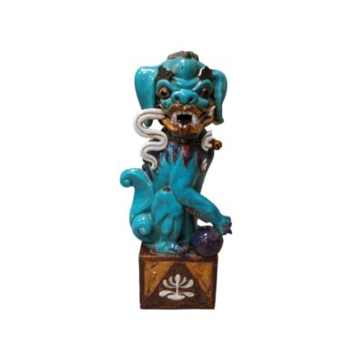 estatuilla de cerámica que representa a un tradicional león guardián o perro de Fu con un llamativo acabado esmaltado en tonos azules y detalles contrastantes, caracterizado por una postura protectora con una pata apoyada sobre una esfera y montado sobre una base cúbica decorada alquiler para eventos, publicidad, peliculas y series