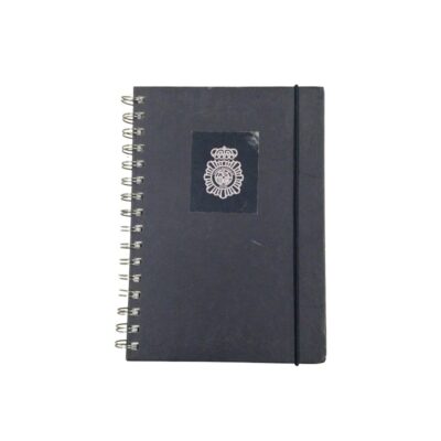A ring-bound notebook with a dark blue cover, featuring a vertical elastic band fastening and bearing the official emblem of the Spanish National Police Force printed in the centre of the front cover; available for hire for events, advertising, films and TV series