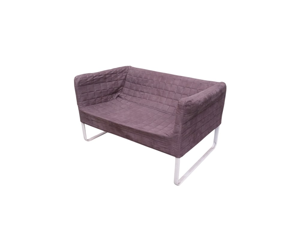 moderno sofá biplaza de época, caracterizado por su cuerpo envolvente tapizado en tejido textil de color gris oscuro con un distintivo diseño acolchado en patrón de cuadrícula, sostenido sobre una robusta estructura de soporte tubular en color blanco alquiler para eventos, publicidad, peliculas y series