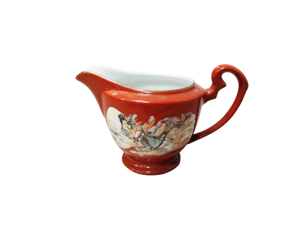 Ceramic milk jug with a pedestal base and a distinctive curved handle on top, characterised by a rich terracotta-coloured exterior glaze and a glossy white interior; available for hire for events, advertising, films and TV series