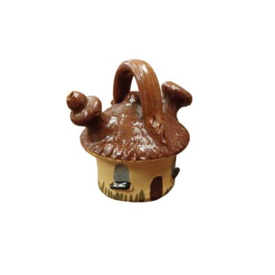 A small ceramic jug modelled in the unique shape of a rustic cottage, featuring a handle at the top, a spout on the side and a glossy brown glaze finish on the top that resembles a roof; available for hire for events, advertising, films and TV series