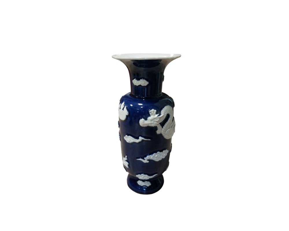 jarrón de porcelana con un acabado esmaltado en tono azul oscuro profundo, caracterizado por un cuerpo cilíndrico, un cuello acampanado y llamativos relieves en color blanco que representan un dragón tradicional entrelazado y motivos de nubes estilizadas a lo largo de su superficie alquiler para eventos, publicidad, peliculas y series