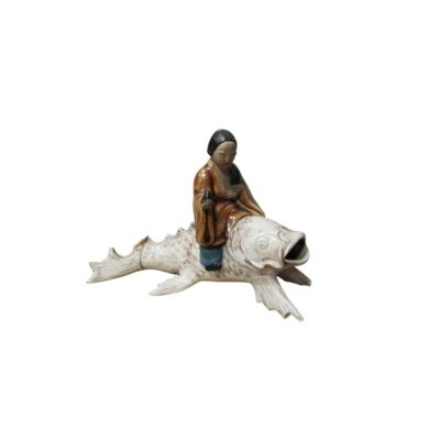 An oriental-inspired decorative ceramic figurine depicting a traditional character dressed in a tunic in shades of brown and ochre, riding on the back of a large, light-coloured fish or carp with detailed fins and an open mouth; available for hire for events, advertising, films and TV series