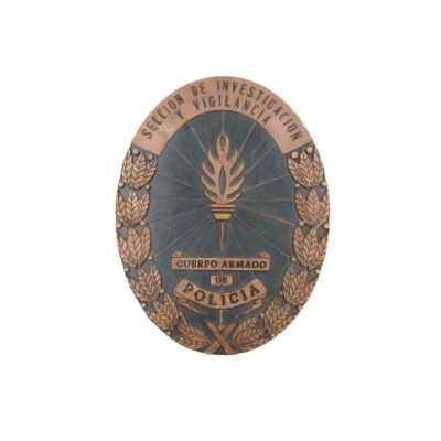 emblema metálico de forma ovalada con acabado envejecido, caracterizada por presentar el diseño de una antorcha central, coronas de hojas de laurel perimetrales y las inscripciones "SECCION DE INVESTIGACION Y VIGILANCIA" junto a "CUERPO ARMADO DE POLICIA" alquiler para eventos, publicidad, peliculas y series