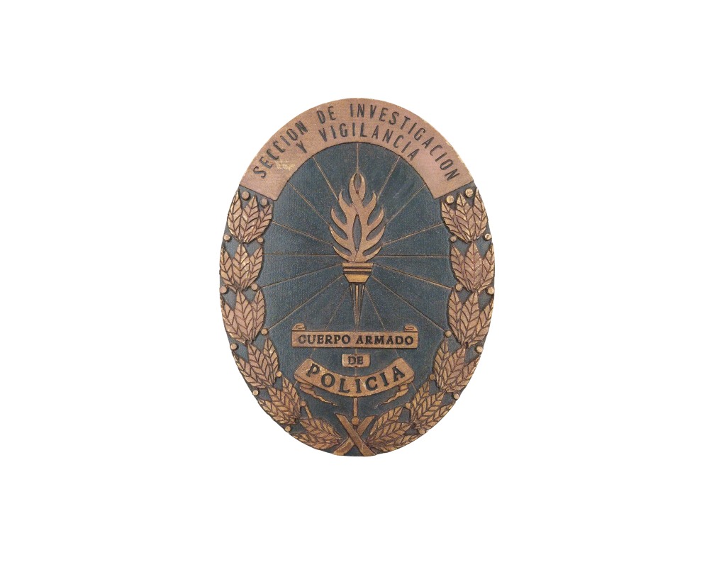 emblema metálico de forma ovalada con acabado envejecido, caracterizada por presentar el diseño de una antorcha central, coronas de hojas de laurel perimetrales y las inscripciones "SECCION DE INVESTIGACION Y VIGILANCIA" junto a "CUERPO ARMADO DE POLICIA" alquiler para eventos, publicidad, peliculas y series