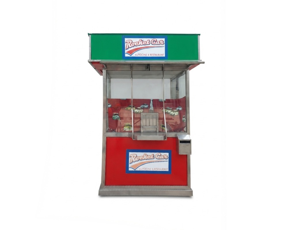 A modular commercial structure or kiosk-style sales booth, designed with a stainless steel frame, glazed panels and plinths in shades of red and green. It features integrated themed signage bearing the slogan ‘Rocket Car Drive-in Cinema & Restaurant – available for hire for events, advertising, films and TV series’.