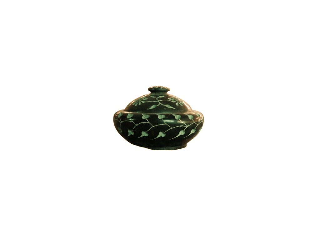 recipiente abombado de color oscuro con tapa a juego, caracterizado por presentar una superficie decorada con finos grabados incrustados en tonos claros que representan motivos florales y enredaderas con hojas alquiler para eventos, publicidad, peliculas y series
