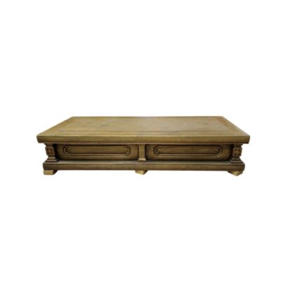 A rectangular, sturdy-looking coffee table in aged brown and gold tones, featuring a spacious top, moulded rectangular panels on the front and architectural legs with small carved details at the corners. Available for hire for events, advertising, films and TV series.