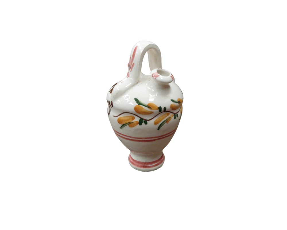 A small glazed ceramic jug in a traditional style, characterised by a tall, slender base, a bulbous body with a handle at the top and a spout, all hand-decorated with floral and plant motifs in shades of yellow, green and reddish tones against a light background. Available for hire for events, advertising, films and TV series.