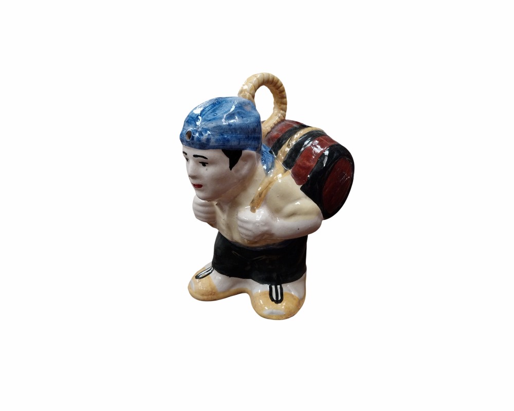 An oriental-inspired ceramic figurine depicting a traditional character, hunched over whilst carrying a barrel tied with ropes on his back, wearing a blue headscarf, a light-coloured shirt and dark trousers; available for hire for events, advertising, films and TV series