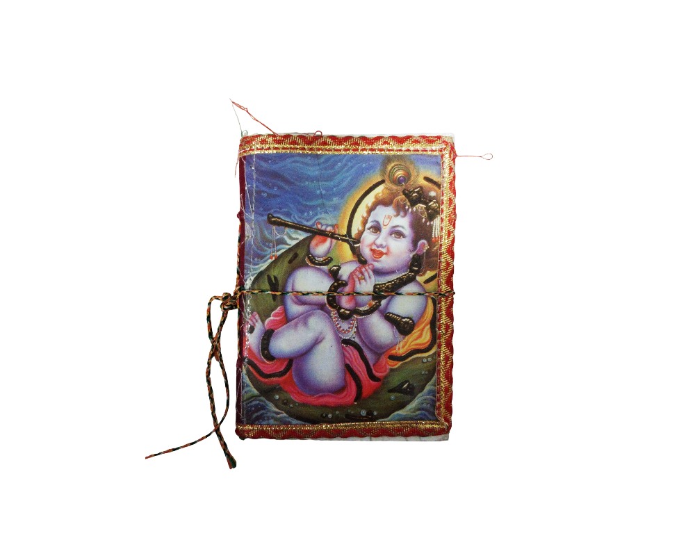Handcrafted notebook in portrait format, featuring a fabric cover decorated with a colourful illustration of a child deity of Hindu inspiration (Krishna) on a floating leaf, framed by gold and red borders, and fitted with a drawstring closure on the side. Available for hire for events, advertising, films and TV series.