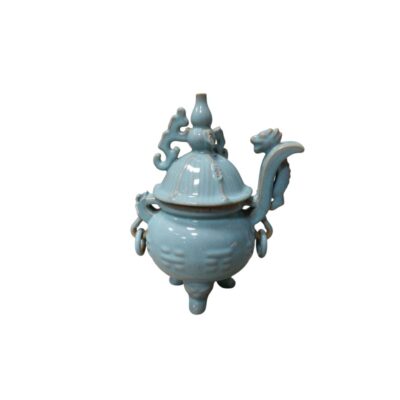recipiente de porcelana con un acabado vidriado en tono verde celadón pálido, caracterizado por un cuerpo globular apoyado sobre tres patas cortas, asas laterales con anillos colgantes y una elaborada tapa superior con relieves ornamentales y una figura zoomorfa erguida alquiler para eventos, publicidad, peliculas y series