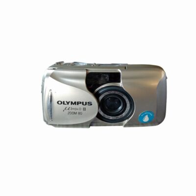 A prestigious compact analogue camera from the renowned Olympus brand, the µ[mju:]-II Zoom 80 All-Weather model, which is highly sought-after amongst collectors of 35mm film cameras. It features an ergonomic and elegant design in a silver finish with an integrated sliding protective cover, a 38–80 mm zoom lens and certification for weather resistance; available for hire for events, advertising, films and TV series.
