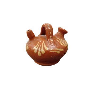 A small ceramic jug with a glossy terracotta-coloured glaze, featuring a handle at the top, a spout and a rim, and hand-decorated with stylised floral and plant motifs in light colours. Available for hire for events, advertising, films and TV series.