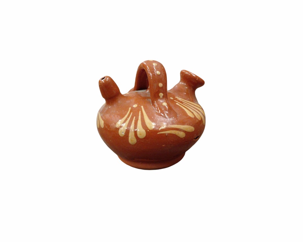 A small ceramic jug with a glossy terracotta-coloured glaze, featuring a handle at the top, a spout and a rim, and hand-decorated with stylised floral and plant motifs in light colours. Available for hire for events, advertising, films and TV series.