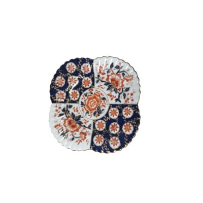 An ornamental plate made of fine porcelain with a lobed silhouette and a distinctive design divided into alternating panels of deep cobalt blue and a white background, richly decorated with floral motifs in reddish tones and accented with fine gold trim around the edges; available for hire for events, advertising, films and TV series