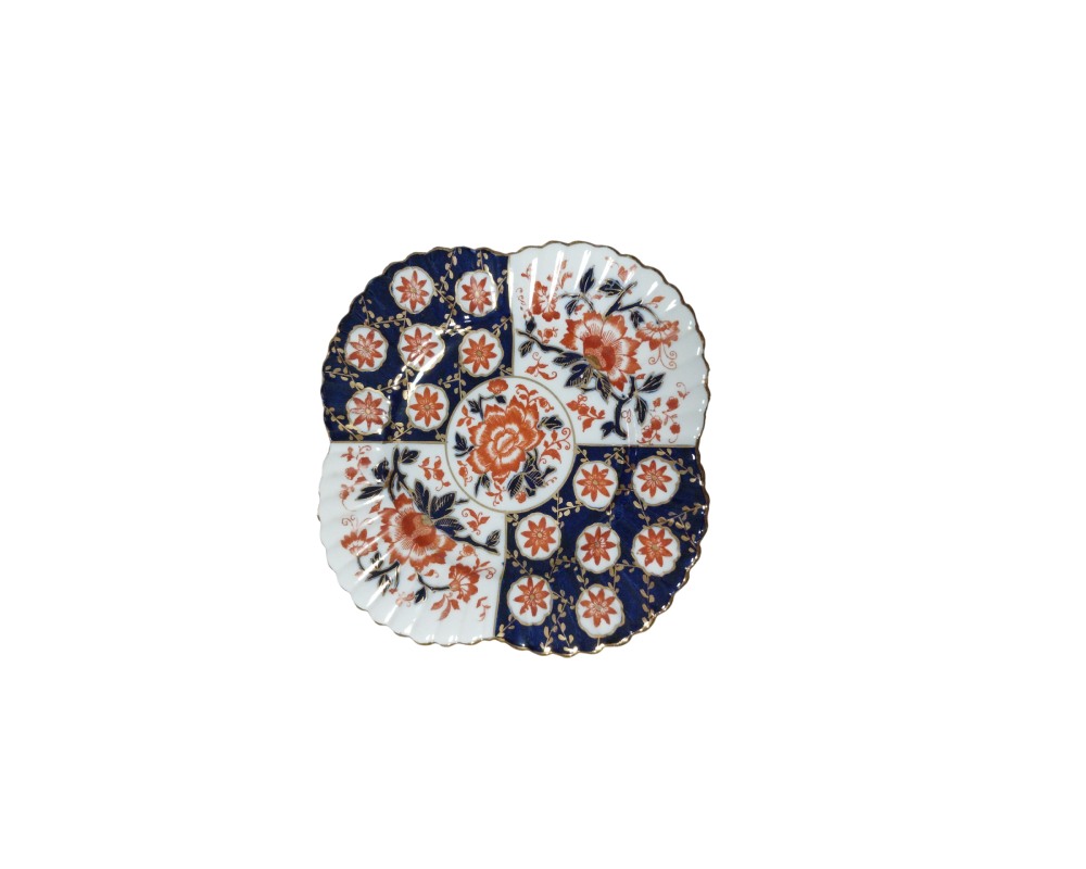 An ornamental plate made of fine porcelain with a lobed silhouette and a distinctive design divided into alternating panels of deep cobalt blue and a white background, richly decorated with floral motifs in reddish tones and accented with fine gold trim around the edges; available for hire for events, advertising, films and TV series