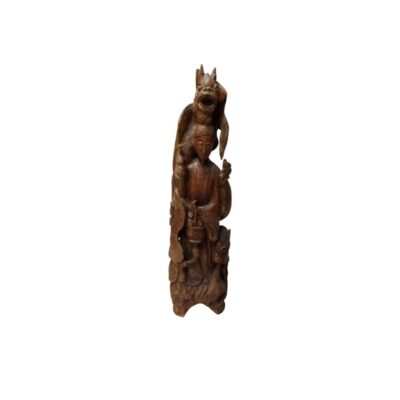 A traditionally styled carved wooden sculpture in shades of brown, characterised by a complex vertical composition depicting a central human figure accompanied by ornamental elements, detailed clothing and mystical creatures; available for hire for events, advertising, films and TV series
