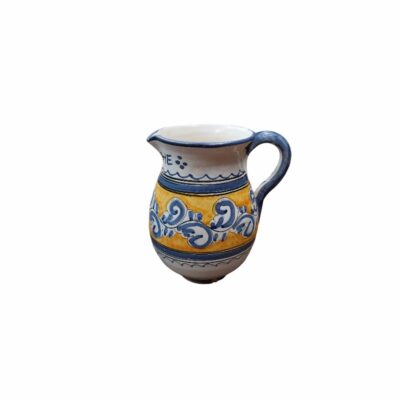 A ceramic milk jug with a rounded body, featuring a side handle, a spout and a surface hand-decorated with bands in ochre tones and plant or spiral motifs in blue on a white background; available for hire for events, advertising, films and TV series