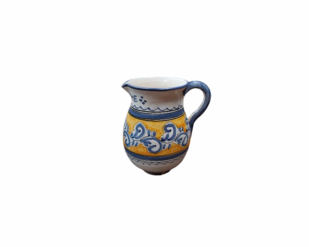 A ceramic milk jug with a rounded body, featuring a side handle, a spout and a surface hand-decorated with bands in ochre tones and plant or spiral motifs in blue on a white background; available for hire for events, advertising, films and TV series