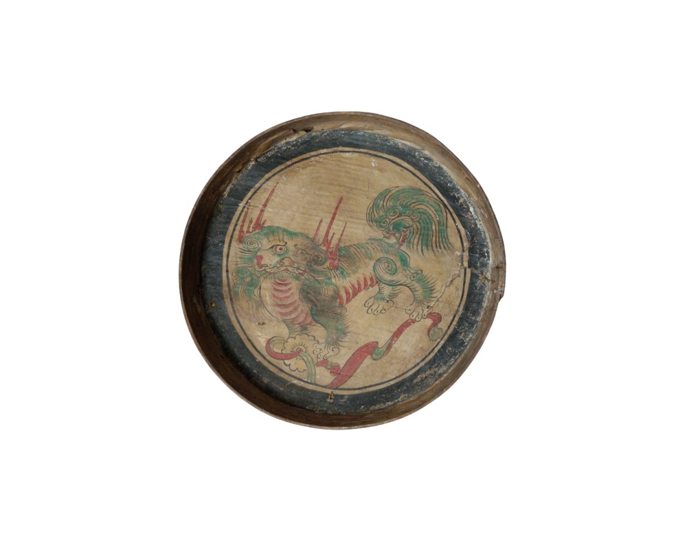 A circular wooden tray, featuring an interior surface decorated with an artistic depiction of a traditional mythological creature in shades of green and red, surrounded by a dark circular border; available for hire for events, advertising, films and TV series