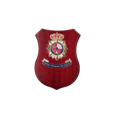 Esta pieza es una metopa decorativa con base de madera en tonos rojizos de diseño heráldico, caracterizada por incorporar el emblema metálico a todo color del Cuerpo Nacional de Policía en la parte superior y una placa o cinta inferior con la inscripción institucional alquiler para eventos, publicidad, peliculas y series