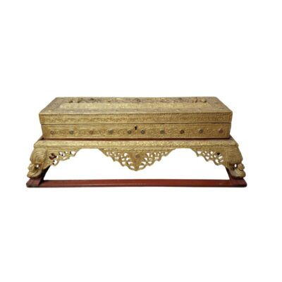 A decorative rectangular chest with a gold finish and intricate relief work, featuring inlays of coloured beads running along its sides and a central lock, resting on an elegant carved base in shades of gold and red; available for hire for events, advertising, films and TV series