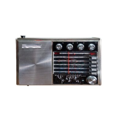 radio portátil de época de estilo clásico, caracterizada por su carcasa rectangular con acabado metálico plateado, una amplia rejilla de altavoz lateral y un complejo panel de sintonía multibanda que incluye múltiples mandos giratorios superiores, botones selectores laterales y un distintivo gráfico mapamundi en la parte inferior del dial alquiler para eventos, publicidad, peliculas y series