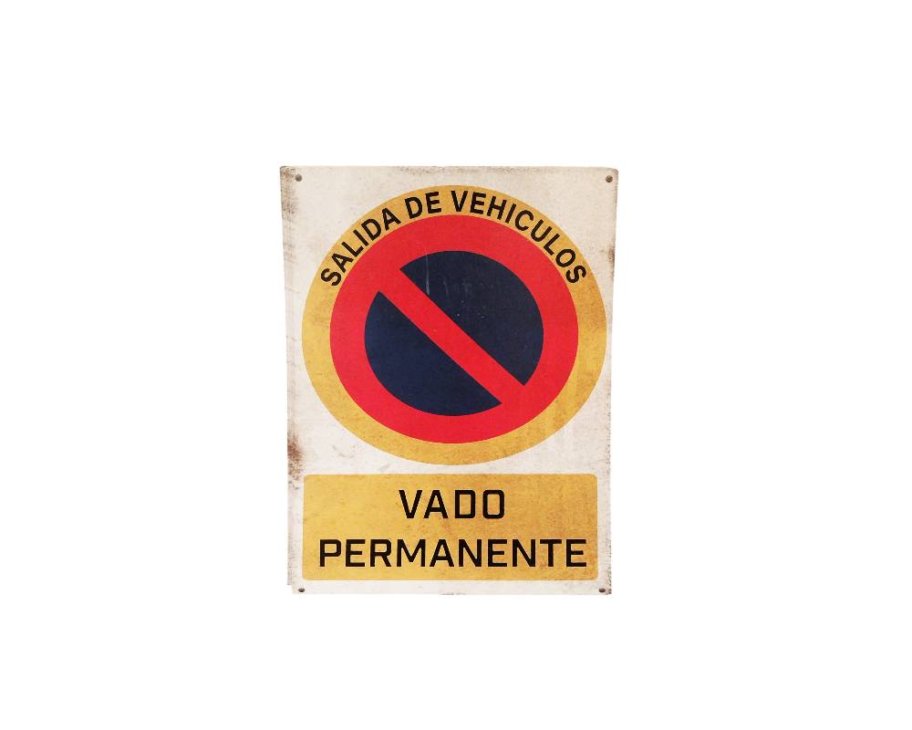 placa rectangular de formato vertical con el diseño clásico de señal de prohibición de estacionamiento, que incluye la leyenda arqueada "SALIDA DE VEHÍCULOS" en la parte superior y el recuadro inferior con el texto "VADO PERMANENTE" alquiler para eventos, publicidad, peliculas y series